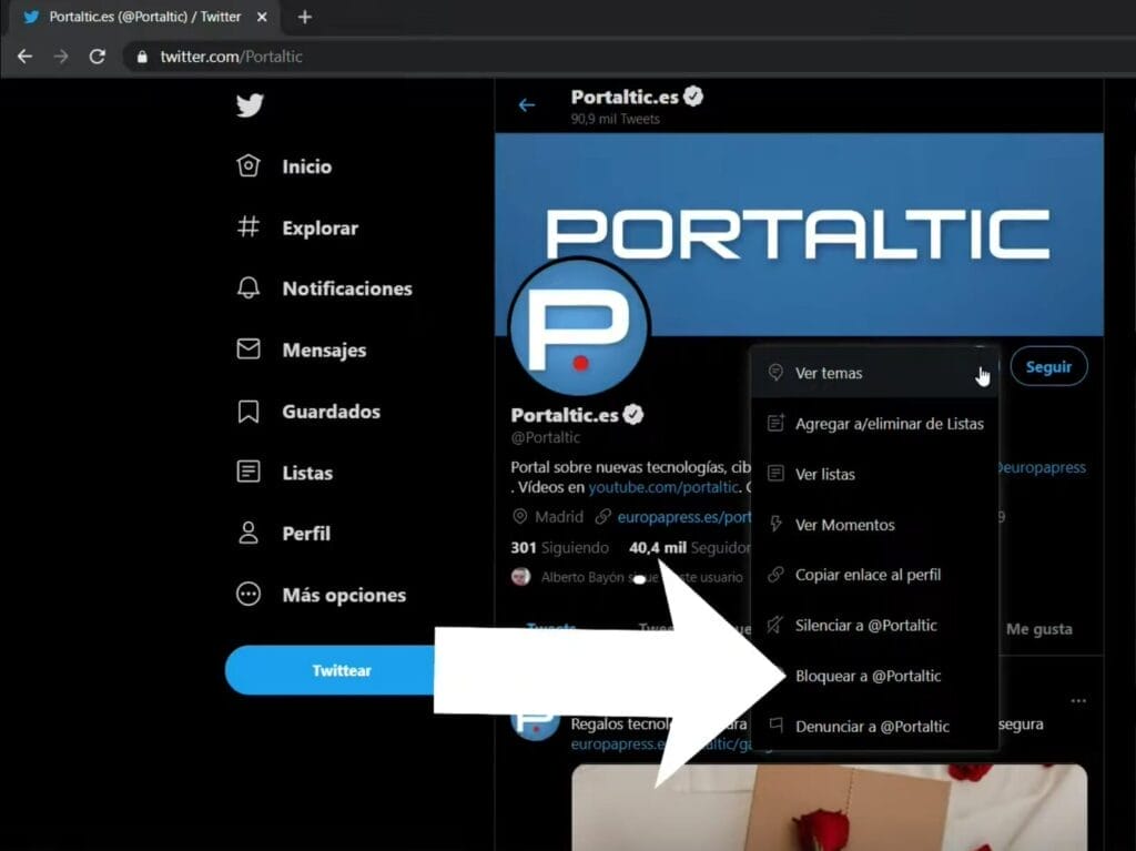 Captura de pantalla de un perfil de Twitter llamado Portalic.es. Se muestra un menú desplegable con opciones que incluyen ver tweets, copiar un enlace al perfil y bloquear o denunciar el perfil (como bloquear un usuario en Twitter). Una flecha se superpone a la imagen.