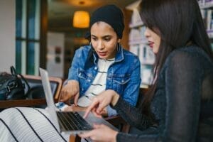 two women looking and pointing at macbook laptop