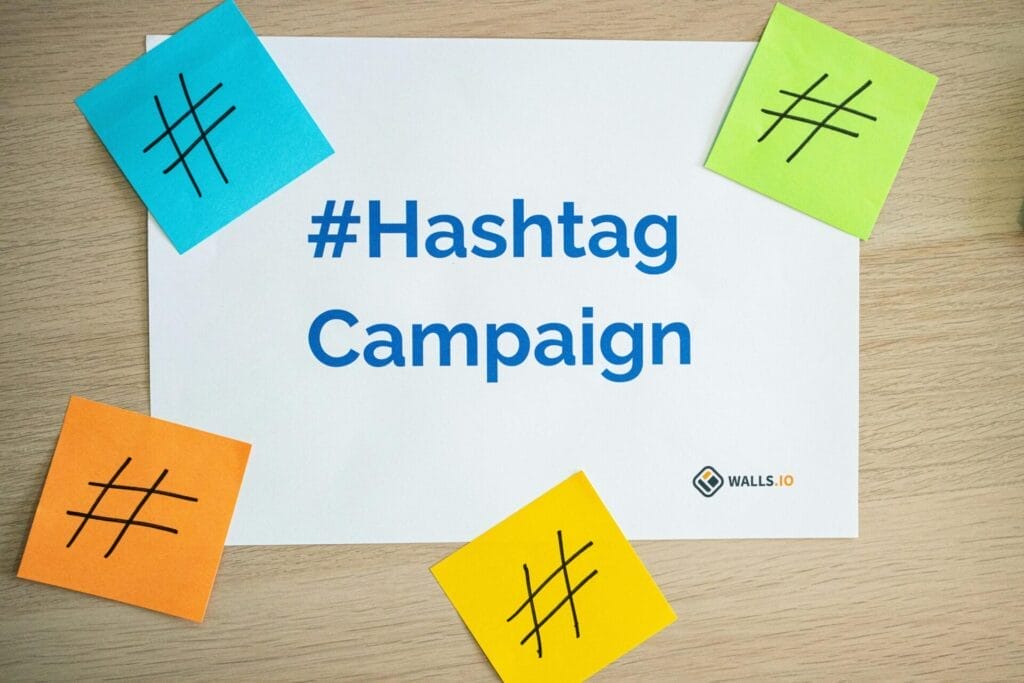 Un papel con la leyenda "#Hashtag Campaign" está rodeado de cuatro notas adhesivas con símbolos de hashtags, que resaltan el poder de los hashtags en Twitter. El logotipo de "walls.io" se encuentra en la esquina inferior derecha.